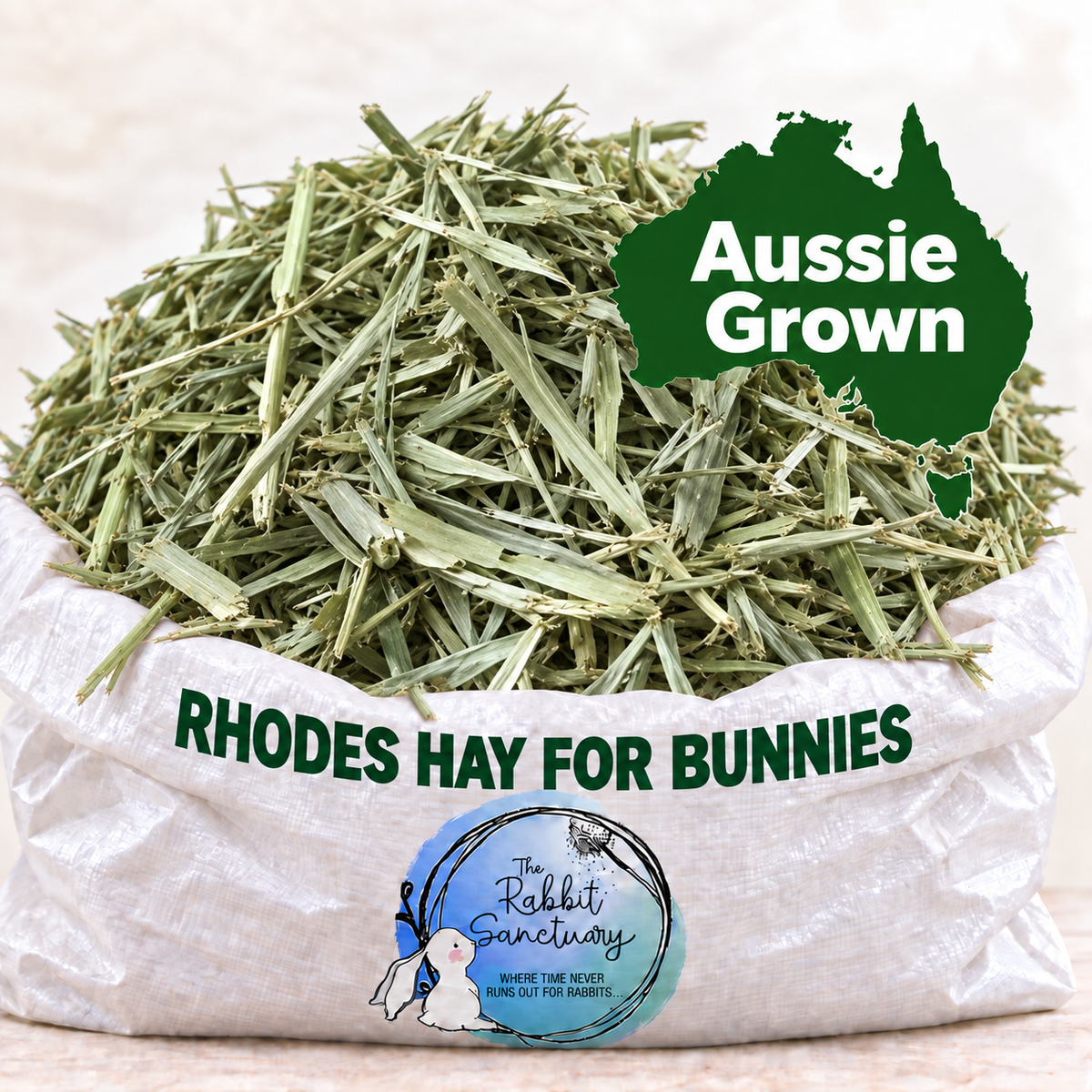 A white paper sack filled with chopped green hay, with a green 'Aussie Grown' label and a circular 'The Rabbit Sanctuary' logo on the sack. The text 'RHODES HAY FOR BUNNIES' is printed across the front.